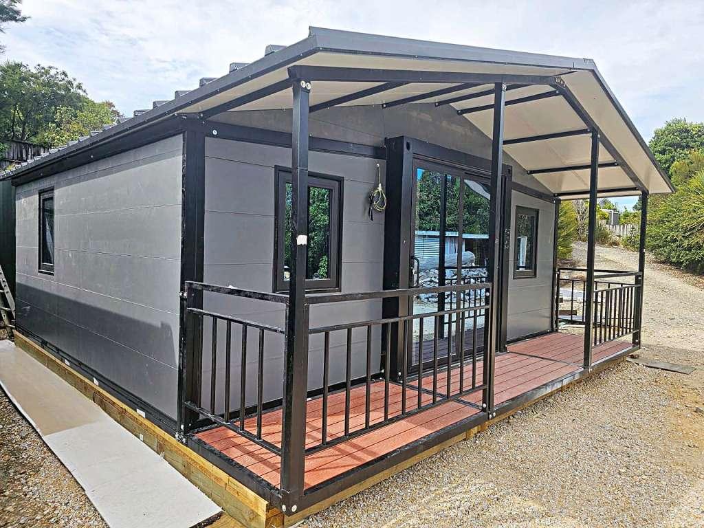Gray and black container home with a gable roof extension, featuring a front deck and railing