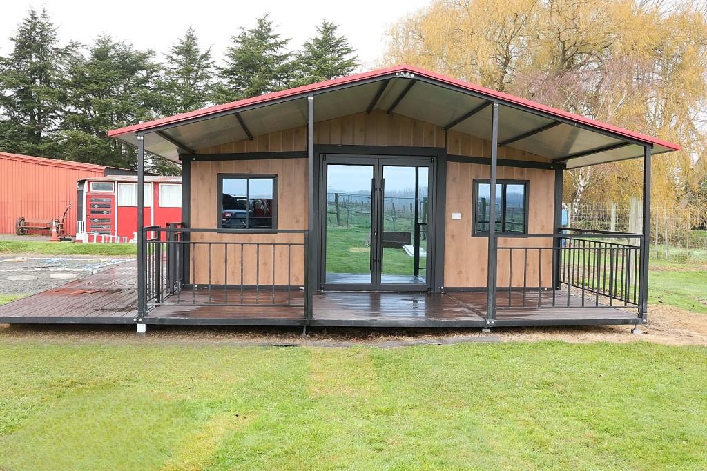 30 ft portable building NZ with cedar-look panels, red gable roof and full-width composite deck on a rural site