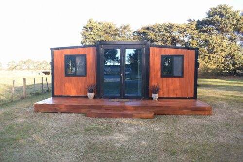 20ft portable house in New Zealand with timber cladding, black aluminium joinery and double doors on a full-width timber deck; hero image for Portable Home NZ Prices